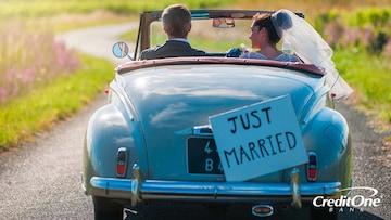 A newly married couple driving away together with a 'Just Married' sign